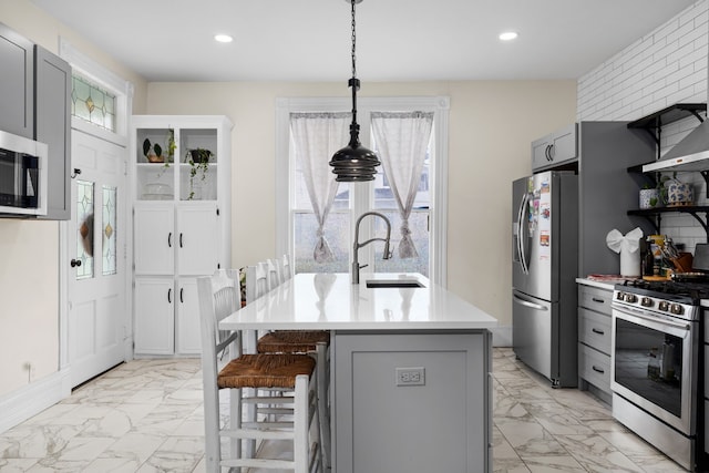 kitchen featuring sink, stainless steel appliances, pendant lighting, gray cabinets, and a center island with sink