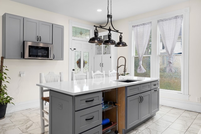 kitchen with gray cabinetry, sink, and an island with sink