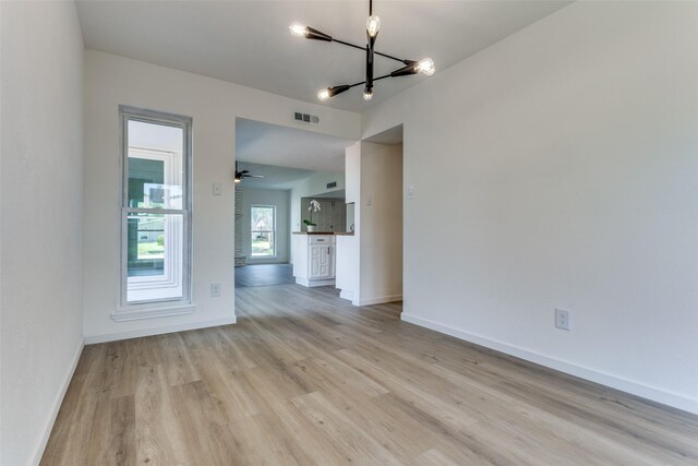 empty room featuring ceiling fan with notable chandelier and light wood-type flooring