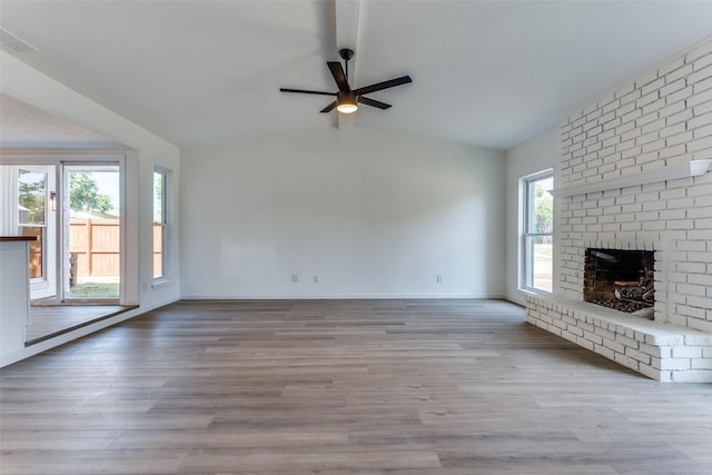 unfurnished living room with lofted ceiling, a fireplace, light hardwood / wood-style floors, and plenty of natural light