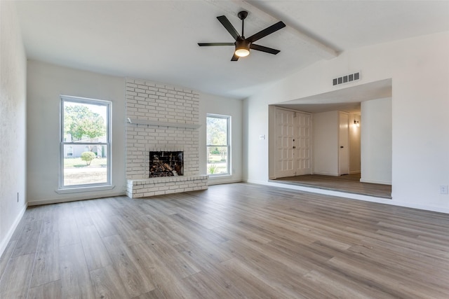 unfurnished living room with a fireplace, light wood-type flooring, lofted ceiling with beams, and plenty of natural light