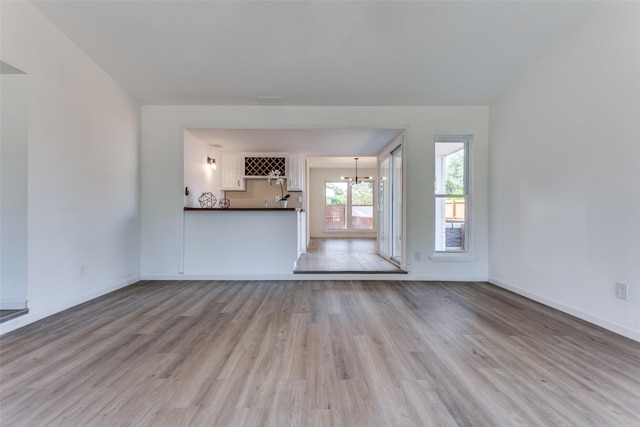 unfurnished living room with light wood-type flooring and an inviting chandelier