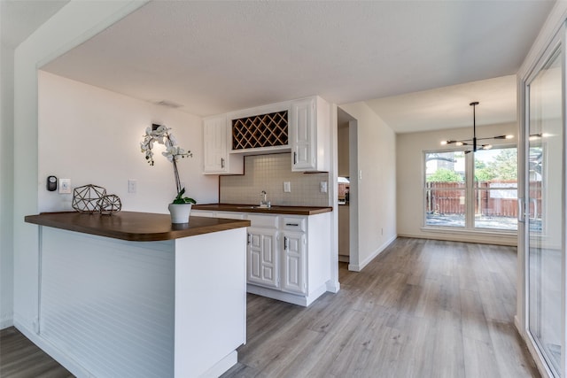 kitchen with kitchen peninsula, tasteful backsplash, an inviting chandelier, white cabinets, and light hardwood / wood-style floors