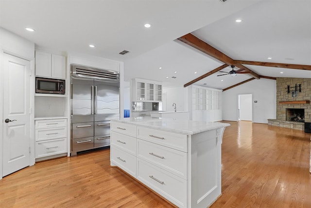 kitchen with vaulted ceiling with beams, a center island, built in appliances, light stone countertops, and white cabinets