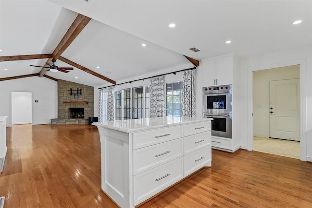 kitchen with double oven, a fireplace, lofted ceiling with beams, white cabinets, and a kitchen island