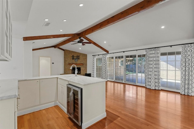 kitchen with lofted ceiling with beams, beverage cooler, kitchen peninsula, and white cabinets