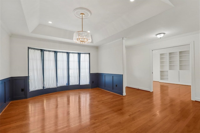 unfurnished room featuring crown molding, an inviting chandelier, hardwood / wood-style floors, built in shelves, and a raised ceiling