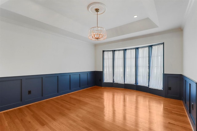 unfurnished room featuring a chandelier, ornamental molding, a raised ceiling, and light hardwood / wood-style flooring