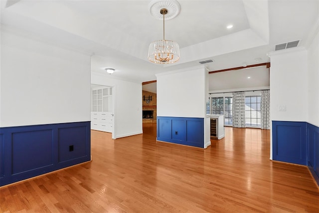 unfurnished room with a raised ceiling, crown molding, a fireplace, and light hardwood / wood-style floors