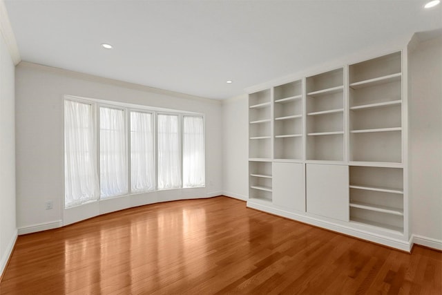 empty room with hardwood / wood-style floors, built in shelves, and ornamental molding