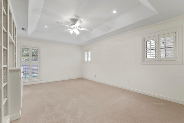 empty room featuring light carpet, a raised ceiling, and ceiling fan