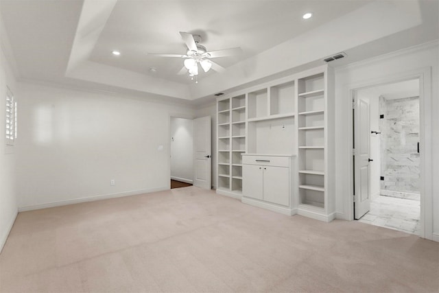 unfurnished bedroom featuring crown molding, ensuite bathroom, a tray ceiling, and light carpet