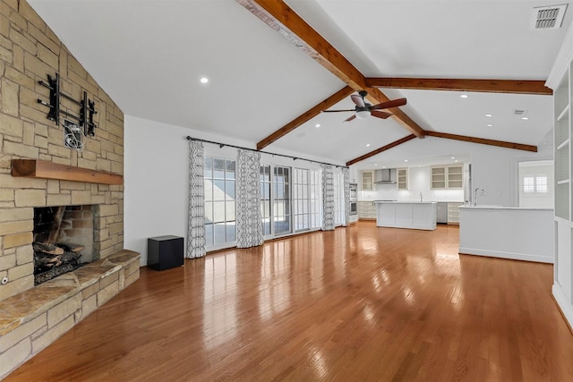 unfurnished living room with sink, a fireplace, light wood-type flooring, and vaulted ceiling with beams