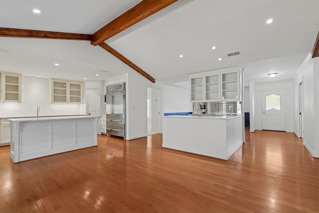 kitchen featuring white cabinetry, vaulted ceiling with beams, backsplash, a center island, and light wood-type flooring