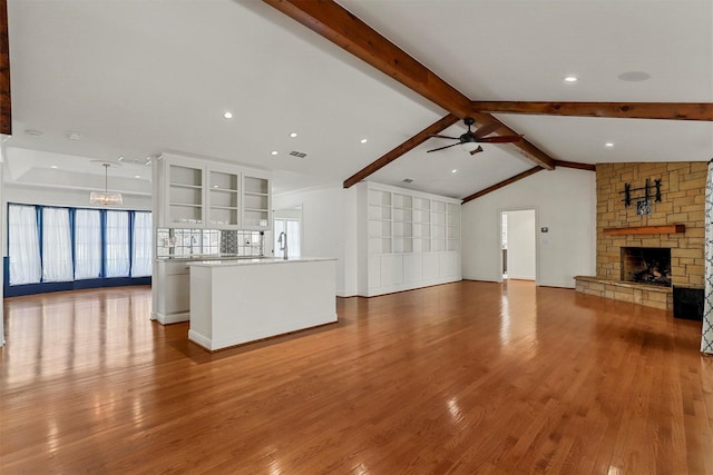 unfurnished living room featuring ceiling fan, a stone fireplace, vaulted ceiling with beams, and light wood-type flooring