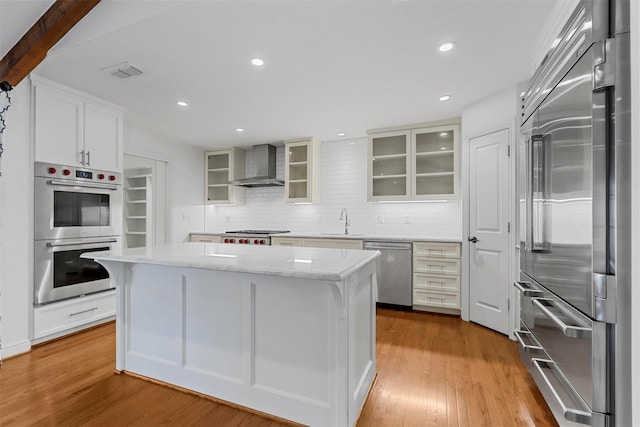 kitchen with light hardwood / wood-style flooring, a kitchen island, wall chimney exhaust hood, and appliances with stainless steel finishes