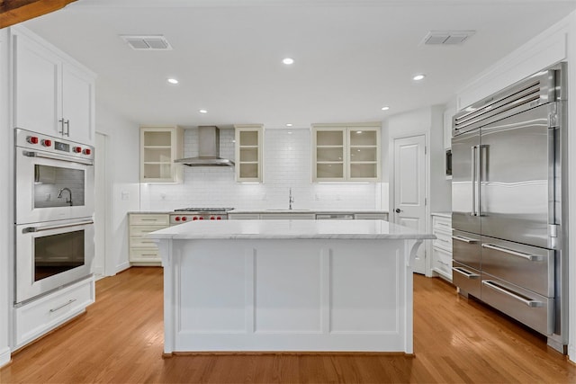 kitchen featuring stainless steel appliances, a center island, white cabinets, and wall chimney exhaust hood