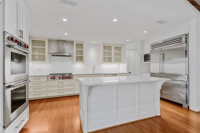 kitchen featuring wall chimney exhaust hood, built in appliances, a center island, and white cabinets