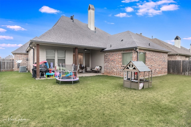 back of property featuring ceiling fan, cooling unit, a patio, a trampoline, and a lawn