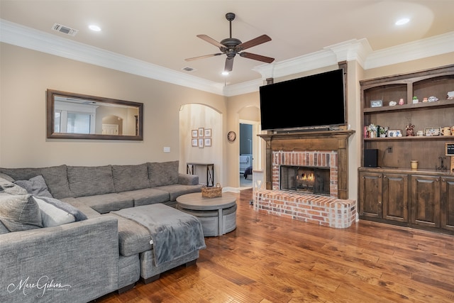 living room featuring a fireplace, wood-type flooring, ceiling fan, and crown molding