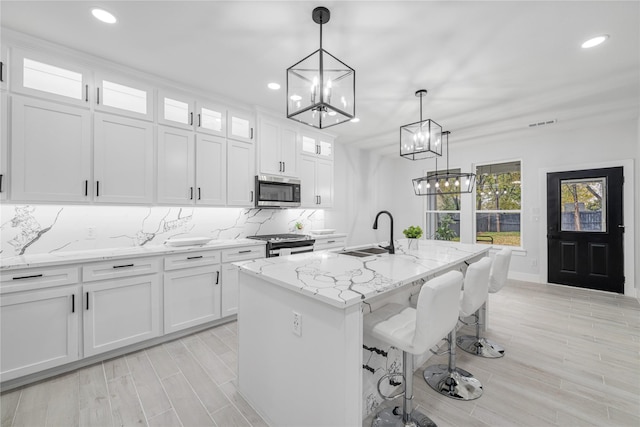 kitchen with white cabinets, stainless steel appliances, a kitchen island with sink, and hanging light fixtures