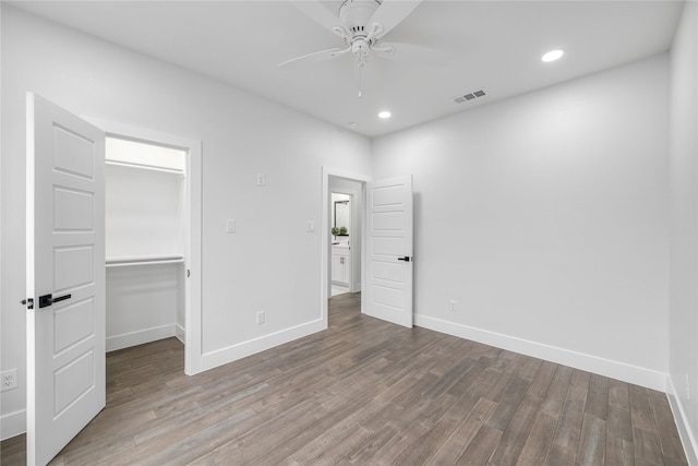 unfurnished bedroom with ceiling fan, wood-type flooring, a spacious closet, and a closet