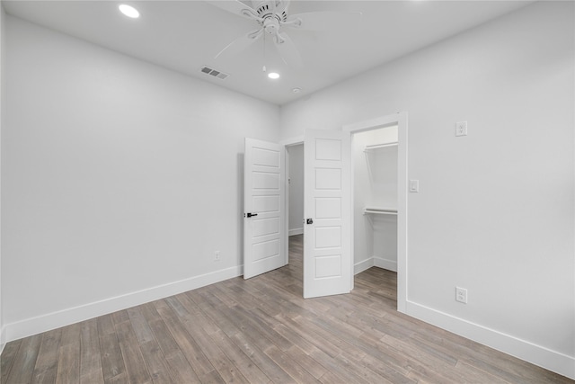 unfurnished bedroom featuring a spacious closet, a closet, ceiling fan, and light wood-type flooring