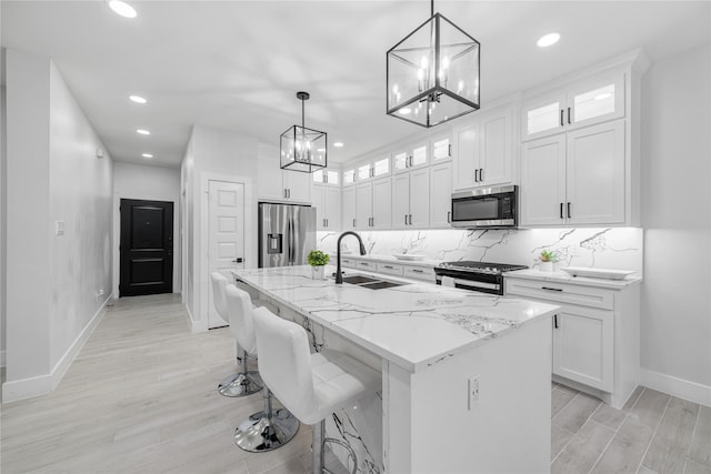 kitchen with a kitchen island with sink, white cabinets, sink, appliances with stainless steel finishes, and decorative light fixtures