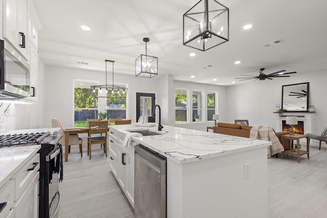 kitchen featuring appliances with stainless steel finishes, a kitchen island with sink, ceiling fan, decorative light fixtures, and white cabinets