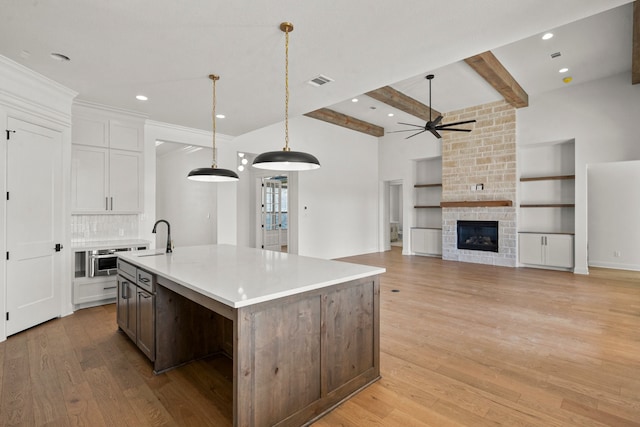 kitchen featuring hanging light fixtures, a center island with sink, beam ceiling, white cabinetry, and ceiling fan