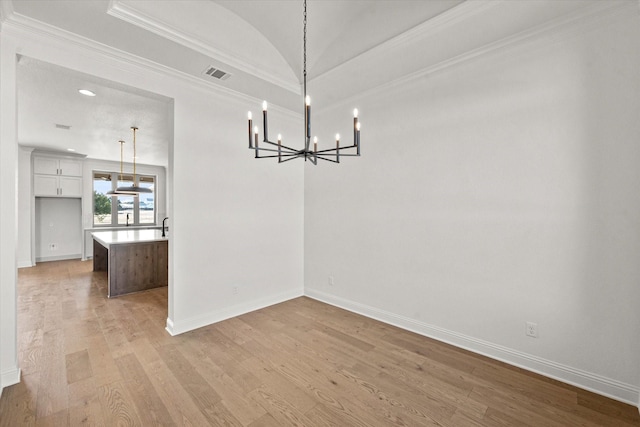 unfurnished dining area with light hardwood / wood-style floors, an inviting chandelier, vaulted ceiling, and crown molding