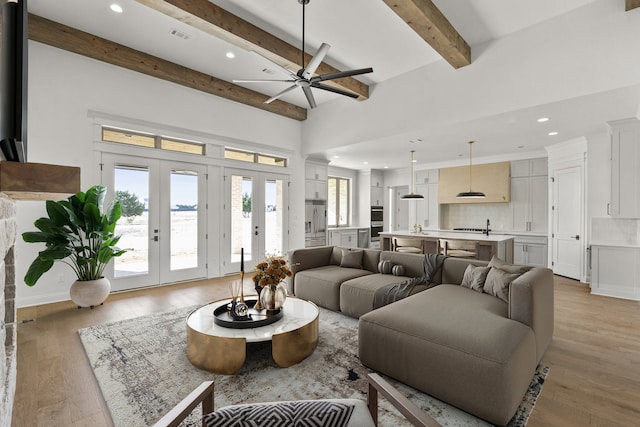 living room featuring ceiling fan, light hardwood / wood-style floors, french doors, and beamed ceiling