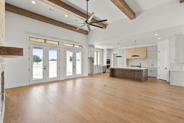 unfurnished living room with a stone fireplace, light wood-type flooring, beamed ceiling, ceiling fan, and french doors