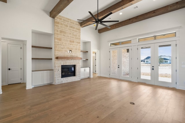 unfurnished living room with french doors, beam ceiling, built in features, ceiling fan, and a stone fireplace