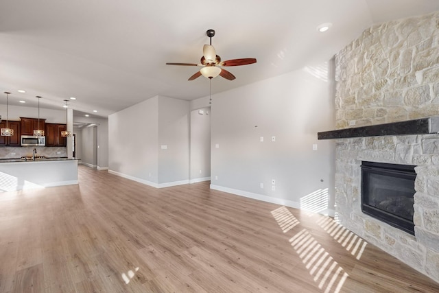 unfurnished living room with a stone fireplace, ceiling fan, and light hardwood / wood-style flooring