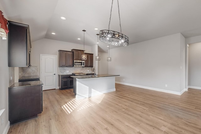 kitchen featuring vaulted ceiling, sink, hanging light fixtures, a kitchen island with sink, and light hardwood / wood-style floors