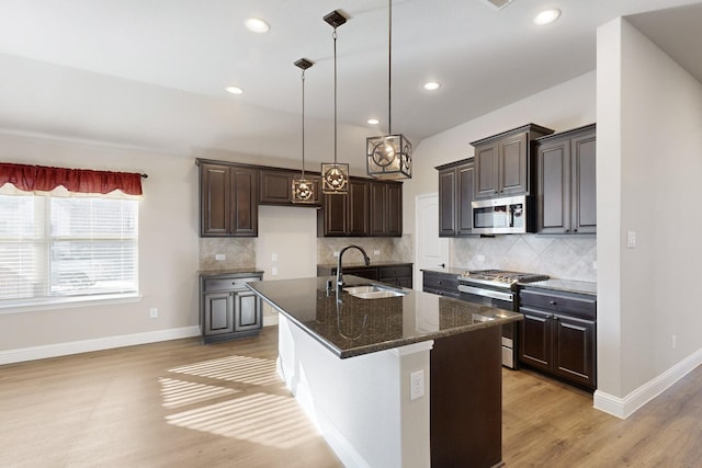 kitchen with sink, appliances with stainless steel finishes, a kitchen island with sink, dark brown cabinetry, and light wood-type flooring