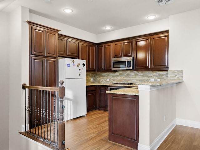 kitchen with decorative backsplash, white refrigerator, light stone countertops, and light hardwood / wood-style flooring