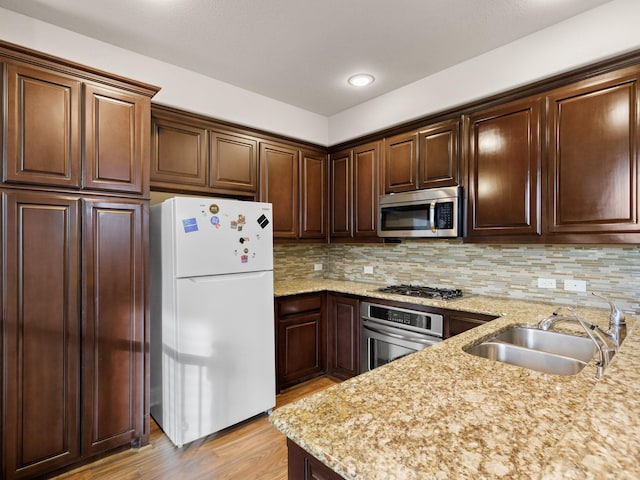 kitchen featuring sink, light stone countertops, appliances with stainless steel finishes, tasteful backsplash, and light hardwood / wood-style floors