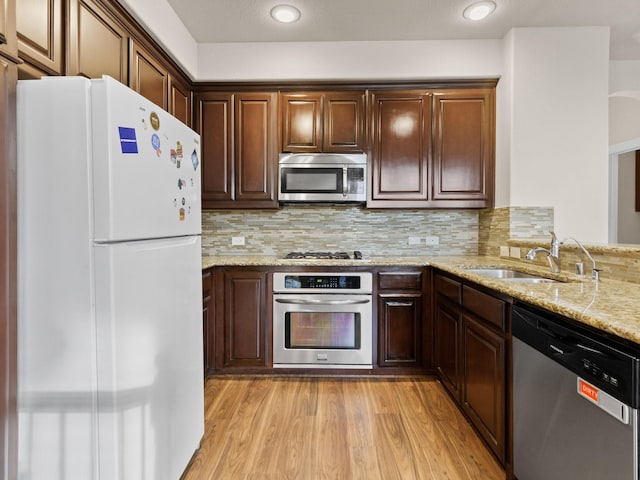 kitchen featuring light stone counters, sink, stainless steel appliances, and light hardwood / wood-style flooring