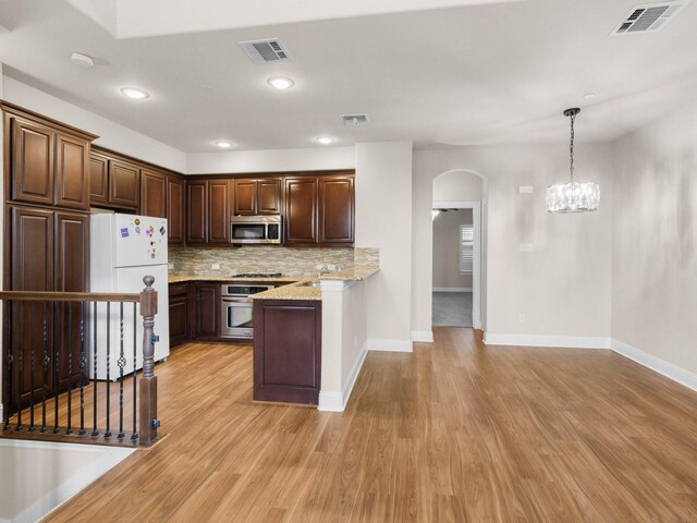 kitchen featuring stainless steel appliances, light stone counters, hanging light fixtures, and light hardwood / wood-style flooring