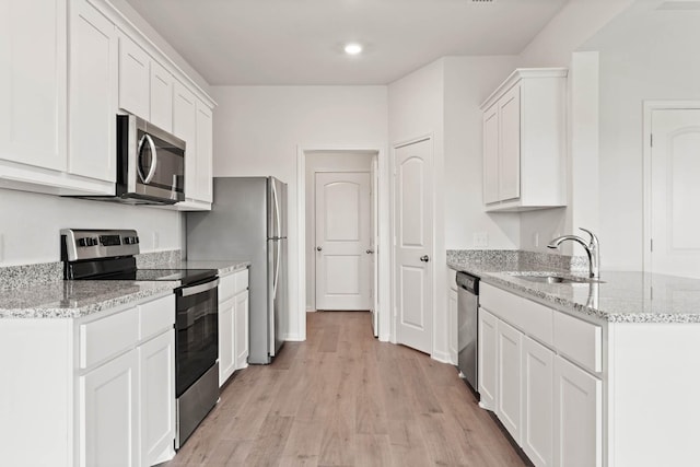 kitchen with sink, white cabinetry, appliances with stainless steel finishes, light stone countertops, and light hardwood / wood-style floors