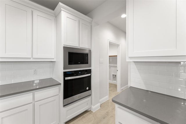 kitchen featuring tasteful backsplash, dark countertops, black microwave, white cabinetry, and stainless steel oven