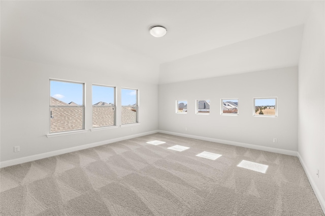 empty room with carpet flooring, baseboards, vaulted ceiling, and a wealth of natural light