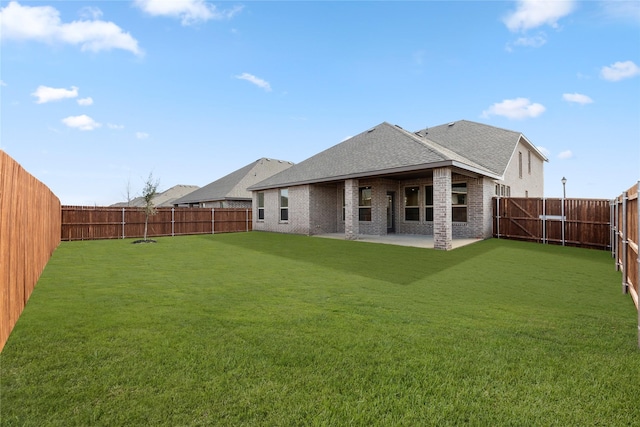 rear view of house with a patio area, a yard, a fenced backyard, brick siding, and roof with shingles