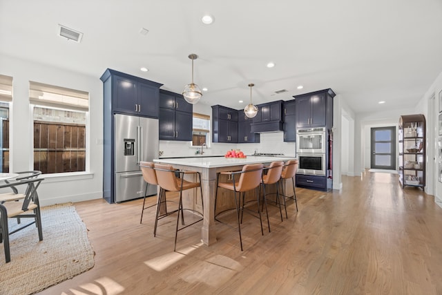 kitchen featuring light hardwood / wood-style flooring, blue cabinetry, appliances with stainless steel finishes, a kitchen island, and a breakfast bar area