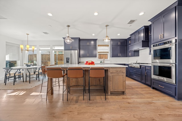 kitchen with a kitchen bar, appliances with stainless steel finishes, light hardwood / wood-style flooring, a kitchen island, and hanging light fixtures