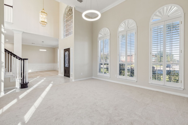 carpeted foyer entrance featuring crown molding, a towering ceiling, and a notable chandelier