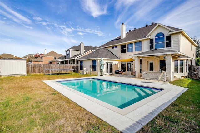 back of property with a lawn, ceiling fan, a trampoline, a fenced in pool, and a patio