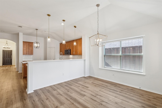 kitchen featuring kitchen peninsula, light wood-type flooring, decorative light fixtures, and vaulted ceiling